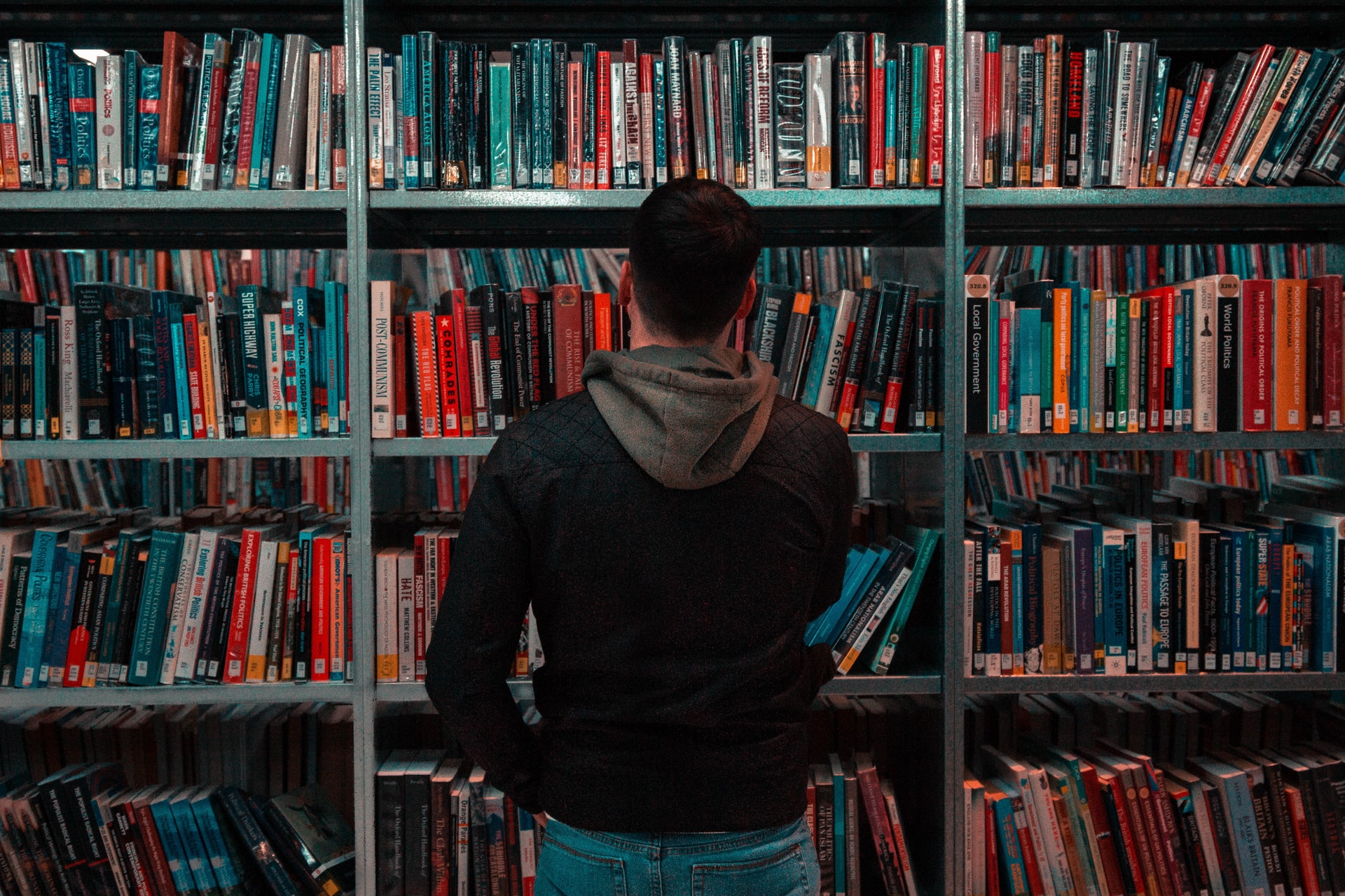 Person wearing black and grey hoodie in front of a bookshelf